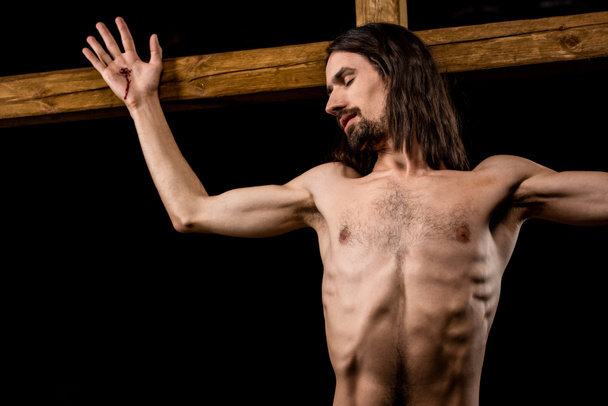Jesus mit geschlossenen Augen gekreuzigt auf Holzkreuz isoliert auf schwarz  - Foto, Bild