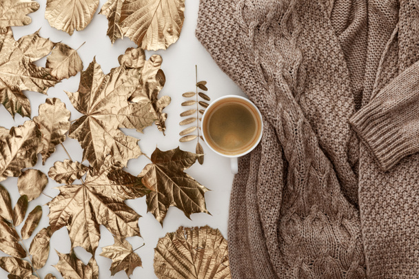 felülnézete kötött barna pulóver, kávé és arany lombozat fehér alapon - Fotó, kép