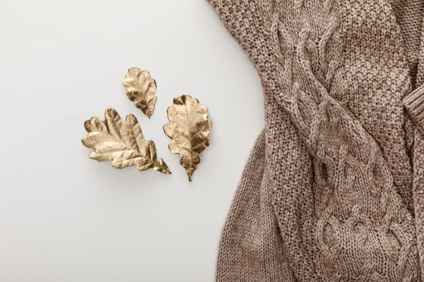 top view of knitted brown sweater and golden leaves on white background - Foto, Imagem