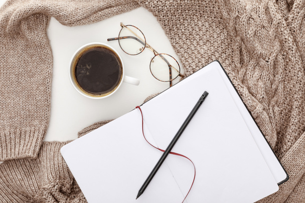 top view of empty notebook, knitted brown sweater, coffee and glasses on white background - Foto, Imagem