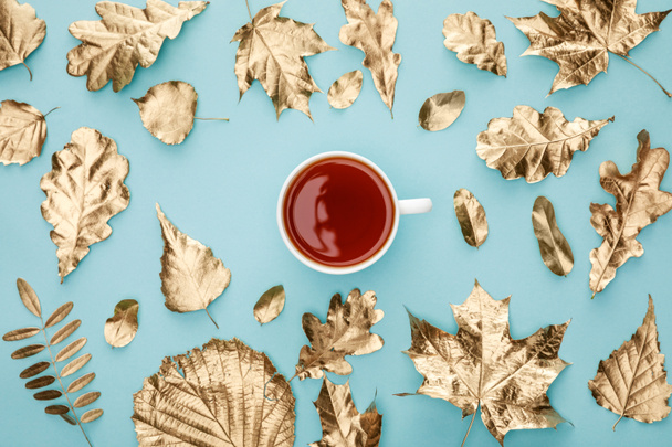 top view of tea in mug near golden foliage on blue background - Foto, immagini