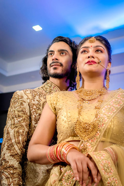 Agosto 2019, Kolkata, India: sposo indiano vestito in Sherwani con splendida sposa in piedi con abiti glamour e gioielli con trucco e tenere ogni mano in una sala banchetti
 - Foto, immagini