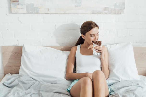 young woman eating chocolate with nuts in bed - Φωτογραφία, εικόνα