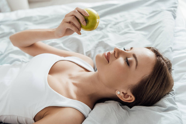 attractive young woman holding green apple in bed - Foto, Imagem