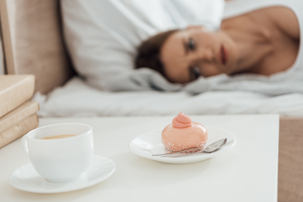 селективный фокус страдающей женщины, лежащей в постели и глядя на кекс
 - Фото, изображение