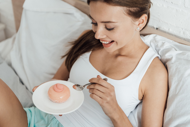 wesoły młoda kobieta leżącego w łóżku i jedzenia Cupcake - Zdjęcie, obraz