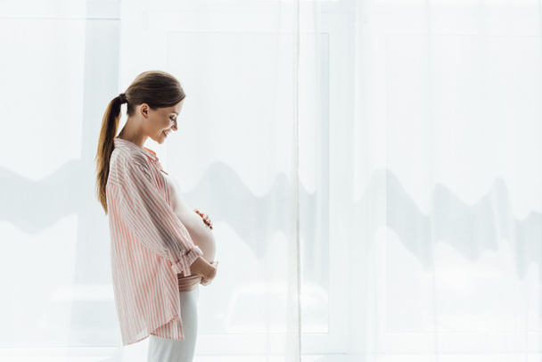 vue latérale de la femme enceinte heureuse sourire et toucher le ventre
 - Photo, image
