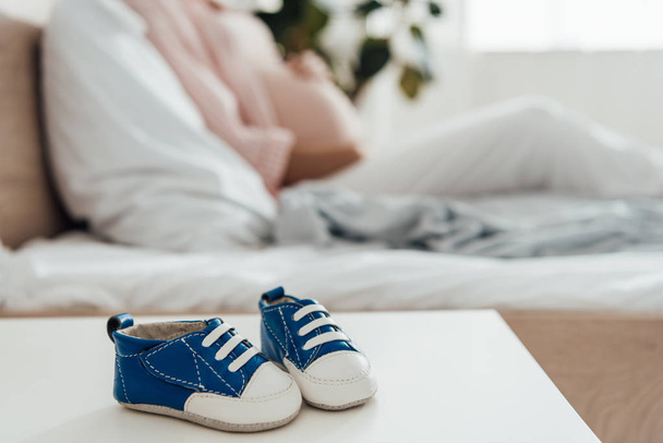 selective focus of pregnant woman and baby shoes on foreground - Photo, Image