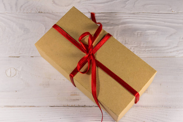 Κουτί δώρου από σκληρό χαρτόνι με κόκκινη κορδέλα στο λευκό ξύλινο τραπέζι - Φωτογραφία, εικόνα