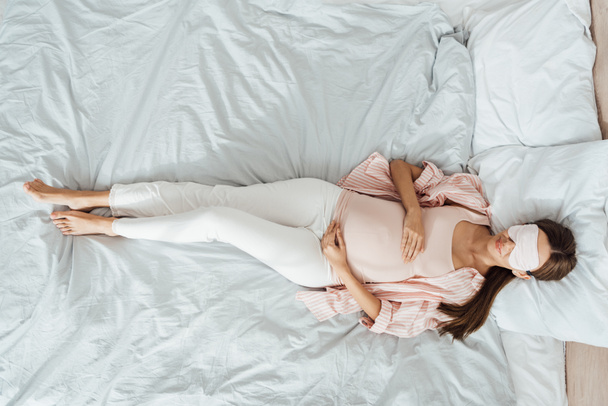 Widok z góry uśmiechnięta kobieta w ciąży leżącej w łóżku i dotykając brzuch - Zdjęcie, obraz