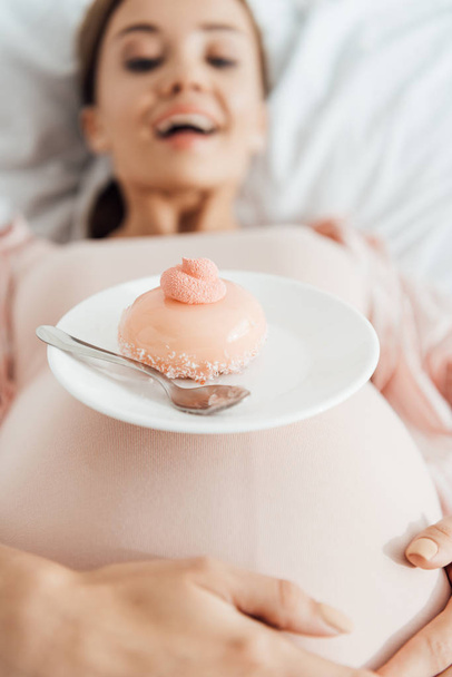 selektivní zaměření těhotné ženy ležící v posteli s koláčem - Fotografie, Obrázek