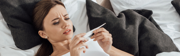 panoramic shot of worried woman lying in bed and looking at pregnancy test - Foto, Imagem