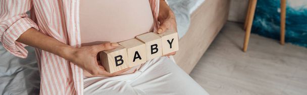 panoramic shot of pregnant woman holding wooden blocks with word baby - Photo, image