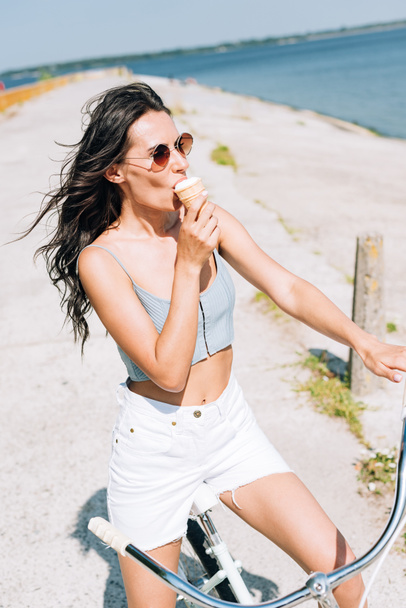 brunetka pojídáním zmrzliny na kole blízko řeky v létě - Fotografie, Obrázek