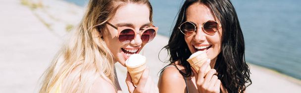 panoramic shot of happy blonde and brunette girls eating ice cream - Foto, imagen