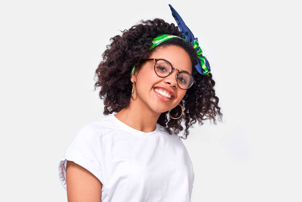 Beautiful happy dark-skinned young woman dressed in white t-shirt, enjoying the weather. African American female smiling broadly, wearing round eyewear posing over white studio wall - Foto, immagini
