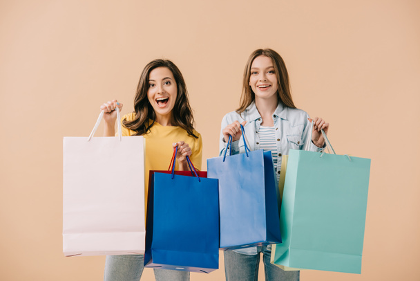 attractive and smiling friends holding shopping bags isolated on beige - Foto, Imagem