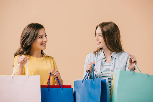 attractive and smiling friends holding shopping bags isolated on beige - Foto, imagen