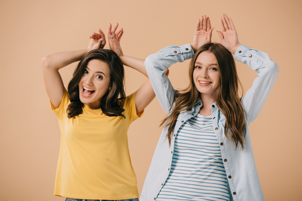 attractive and smiling friends showing bunny ears with hands isolated on beige  - Foto, Imagem