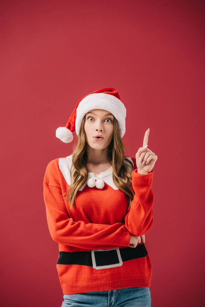 attractive woman in santa hat and sweater showing idea gesture isolated on red  - 写真・画像
