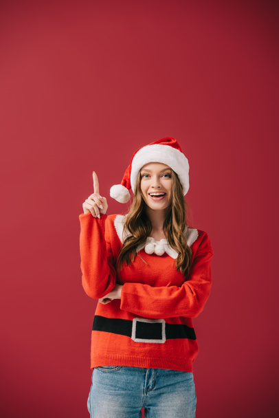 attractive woman in santa hat and sweater showing idea gesture isolated on red  - Fotoğraf, Görsel