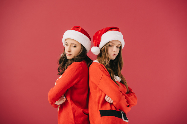 attractive and sad women in sweaters and santa hats looking down isolated on red  - Photo, Image