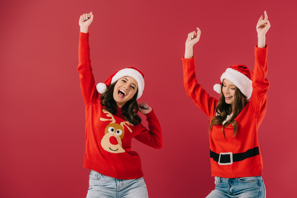 jolies et souriantes femmes en chandails et chapeaux de Père Noël avec les mains tendues isolées sur rouge
  - Photo, image