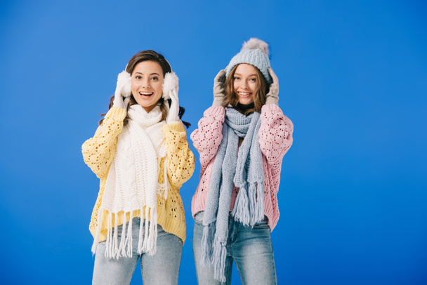 attractive and smiling women in sweaters and scarves looking at camera isolated on blue - Photo, Image