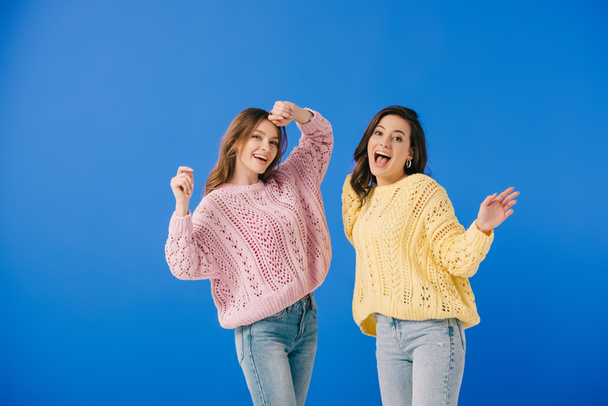 attractive and smiling women in sweaters looking at camera isolated on blue - Фото, изображение