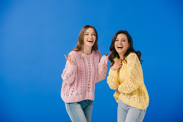 attractive and smiling women in sweaters looking at camera isolated on blue  - Фото, изображение