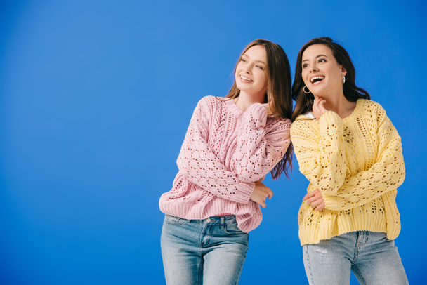 attraktive und lächelnde Frauen in Pullovern, die vereinzelt auf blau wegschauen  - Foto, Bild
