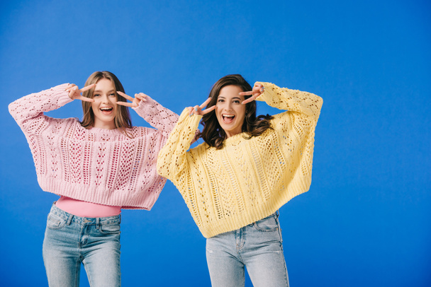attractive and smiling women in sweaters showing victory signs isolated on blue  - Φωτογραφία, εικόνα