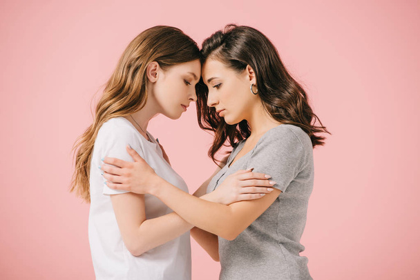 side view of attractive and sad women in t-shirts hugging isolated on pink - Фото, изображение