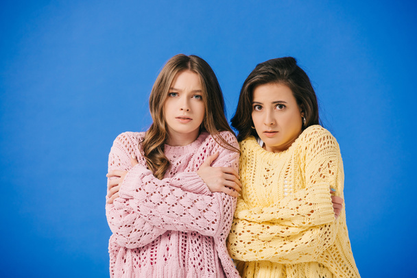 mujeres atractivas en suéteres mirando a la cámara y sintiendo frío aislado en azul
  - Foto, Imagen
