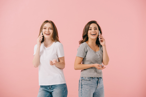 attractive and smiling women in t-shirts talking on smartphones isolated on pink - Фото, зображення