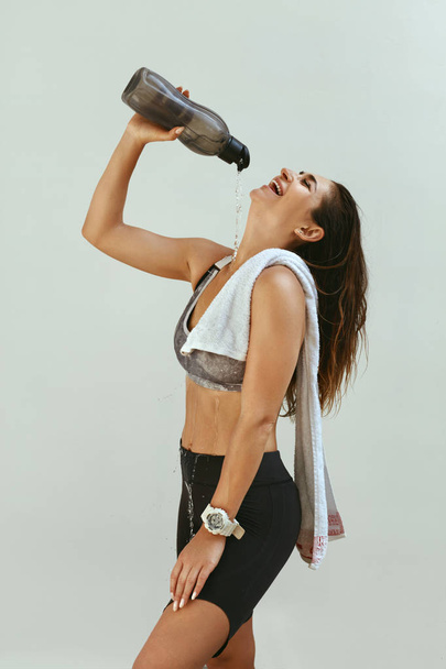 Woman in sports clothing pouring water on body after workout - Foto, Imagen