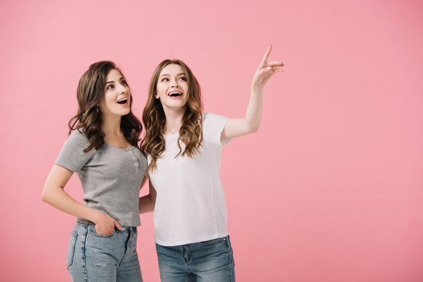 aantrekkelijke en lachende vrouwen in t-shirts wijzend met de vinger geïsoleerd op roze - Foto, afbeelding