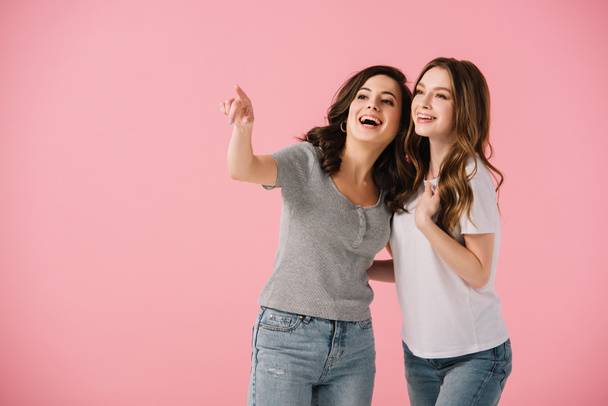 attractive and smiling women in t-shirts pointing with finger isolated on pink - Photo, Image