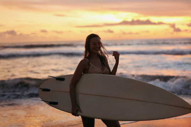 Summer. Surfer girl silhouette with surf board on sunset beach - Foto, Imagem