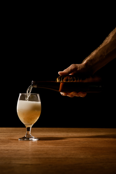 vista parziale dell'uomo versare birra da bottiglia in vetro su tavolo di legno isolato su nero
 - Foto, immagini