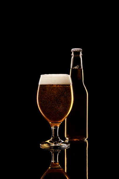 bottle and glass of beer with white foam isolated on black - Foto, immagini