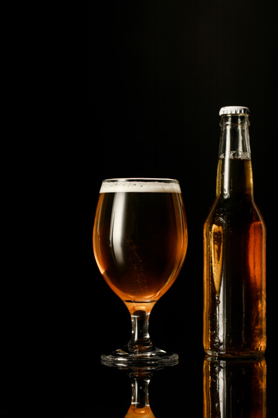 glass of beer with foam near bottle isolated on black - Photo, image