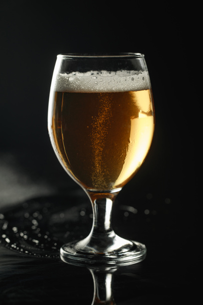glass of beer with foam on wet surface isolated on black - Photo, Image