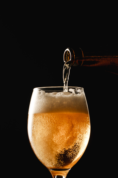 beer flowing from bottle into glass and making foam isolated on black - Foto, Imagem