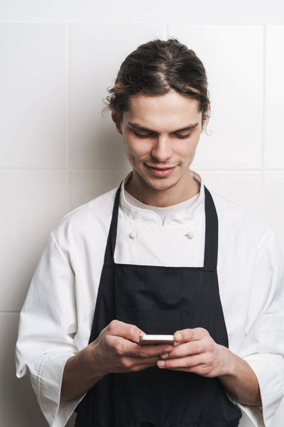 Młody kucharz kucharza w kuchni za pomocą telefonu komórkowego rozmowy. - Zdjęcie, obraz