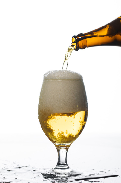 birra versata dalla bottiglia in vetro sulla superficie con pozzanghera isolata su bianco
 - Foto, immagini