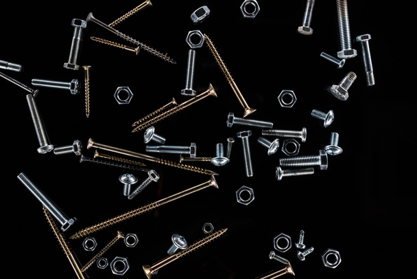top view of scattered nuts, bolts and studs isolated on black - Foto, Imagem