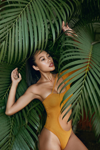 Summer fashion. Woman model in swimsuit near palm leaves - Fotoğraf, Görsel