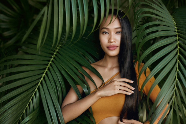 Hair beauty. Woman model with long straight hair in palm leaves - Foto, Imagen