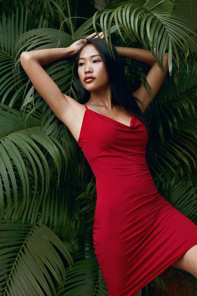 Fashion. Woman model in red dress with green palm leaves - Fotoğraf, Görsel